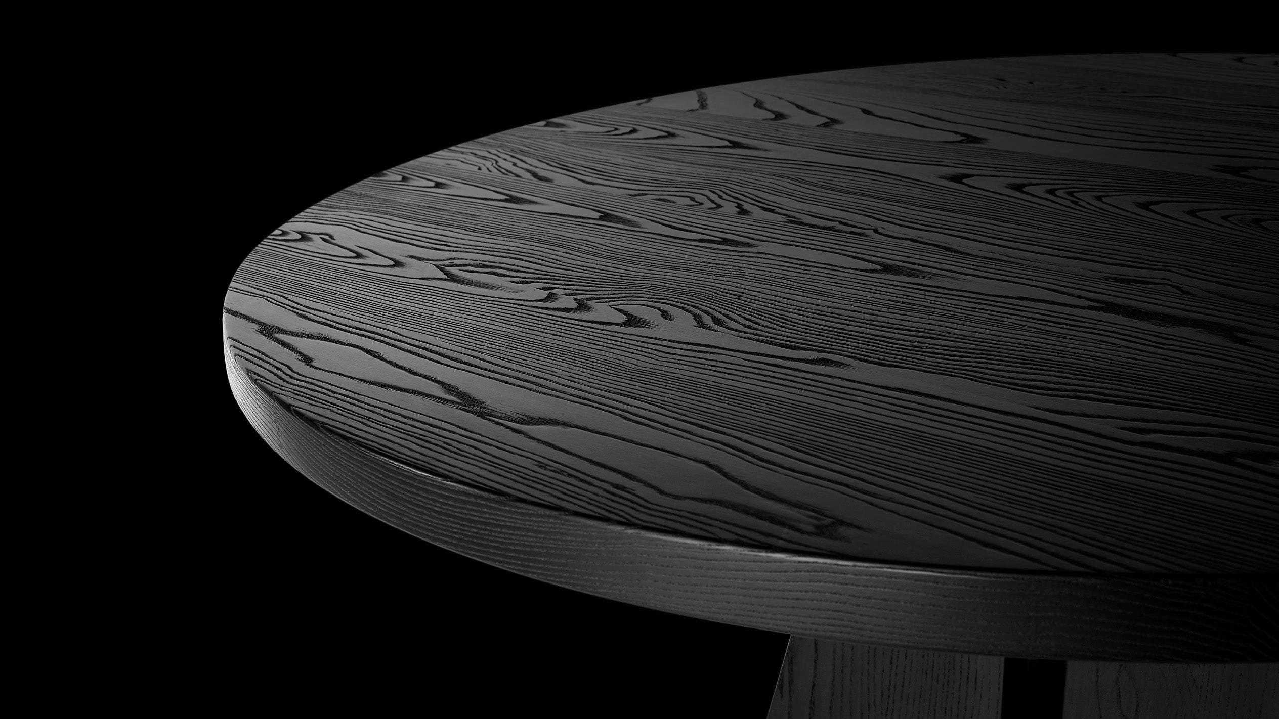 Close up of the circular top of the PORTAL dining table showing details of the Blackened Ash Wood.