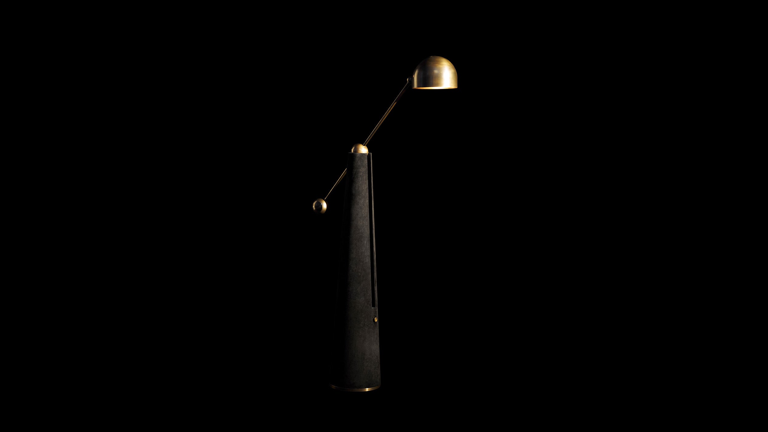 METRONOME reading lamp in Aged Brass finish with Black Suede standing in front of a black background. 
