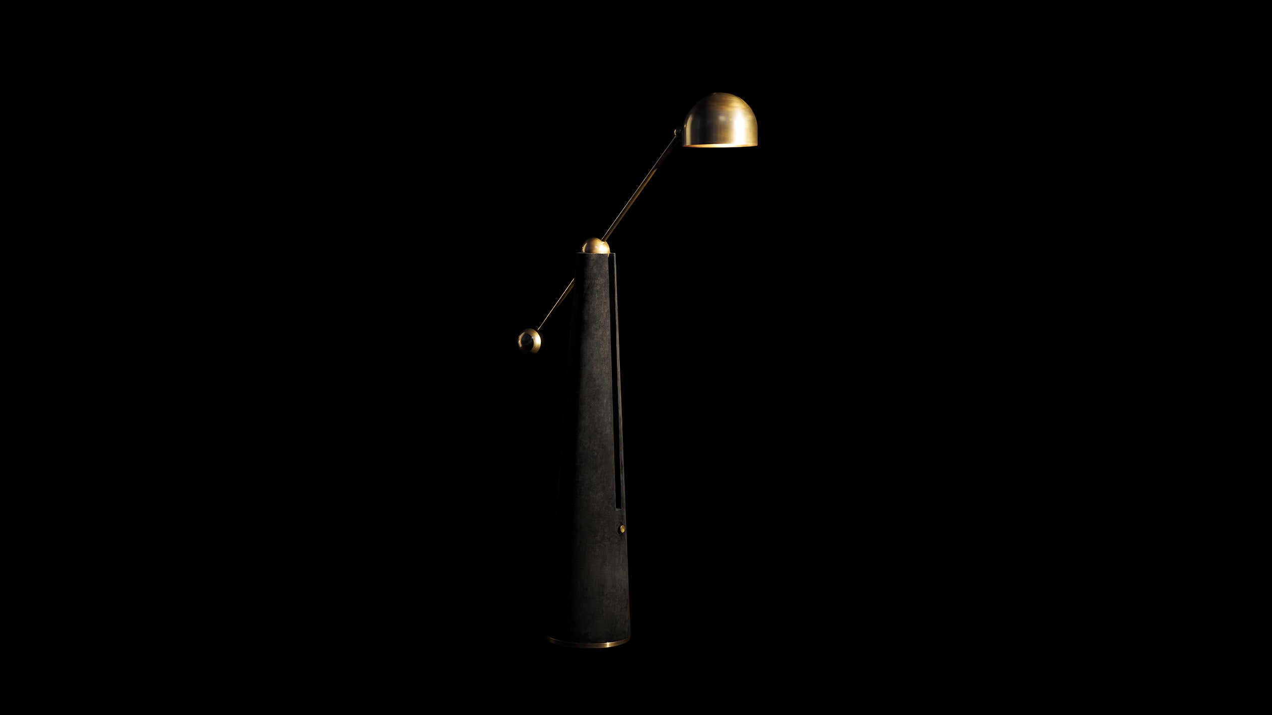 METRONOME reading lamp in Aged Brass finish with Black Suede standing in front of a black background.