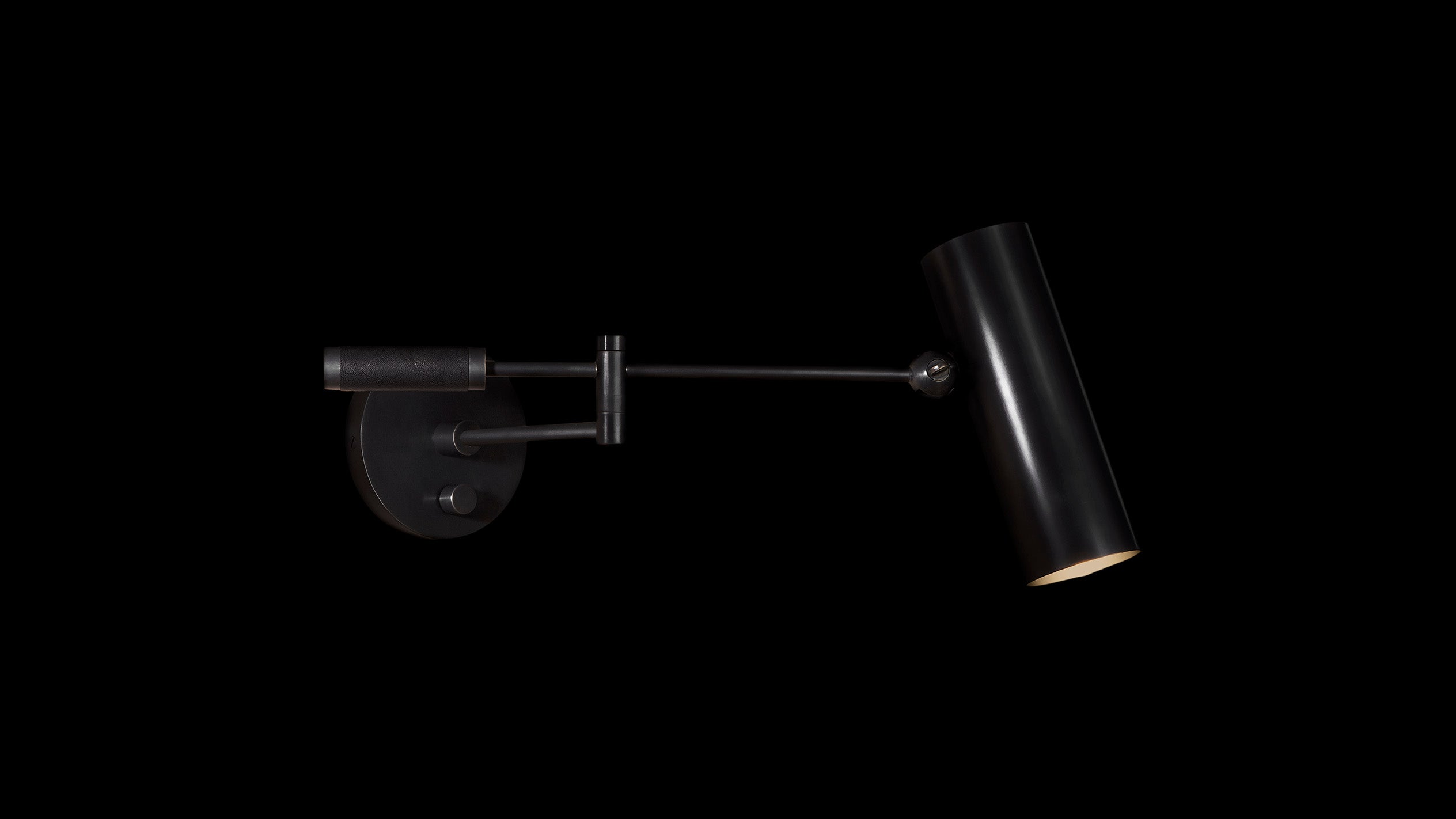 Articulating CYLINDER reading sconce in Blackened Brass and Black Leather, mounted to a black wall.