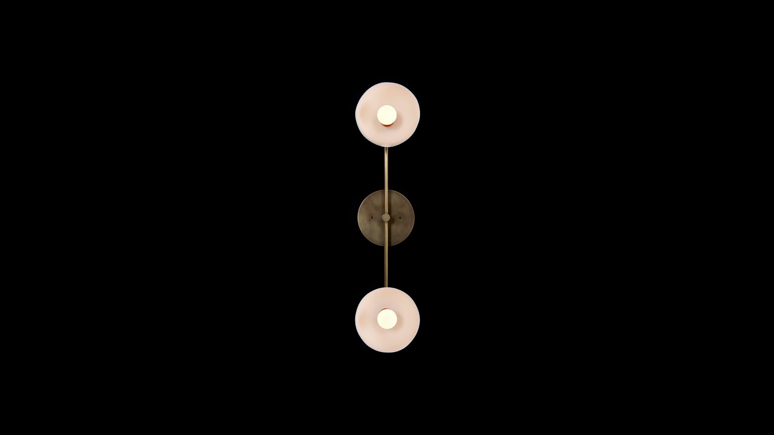 TRAPEZE : 2 surface light in Aged Brass finish with Porcelain bowls, mounted vertically to a black wall. 