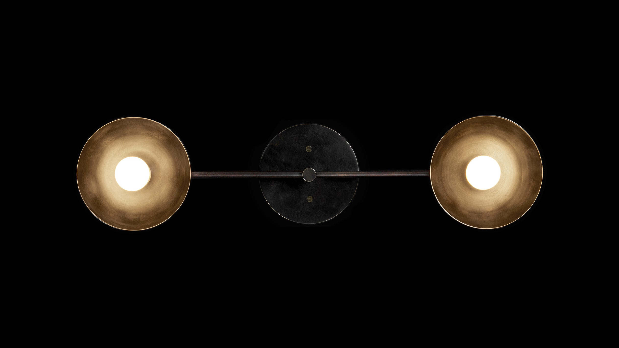 TRAPEZE : 2 surface light in Blackened Brass with Aged Brass bowls, mounted horizontally on a black wall. 