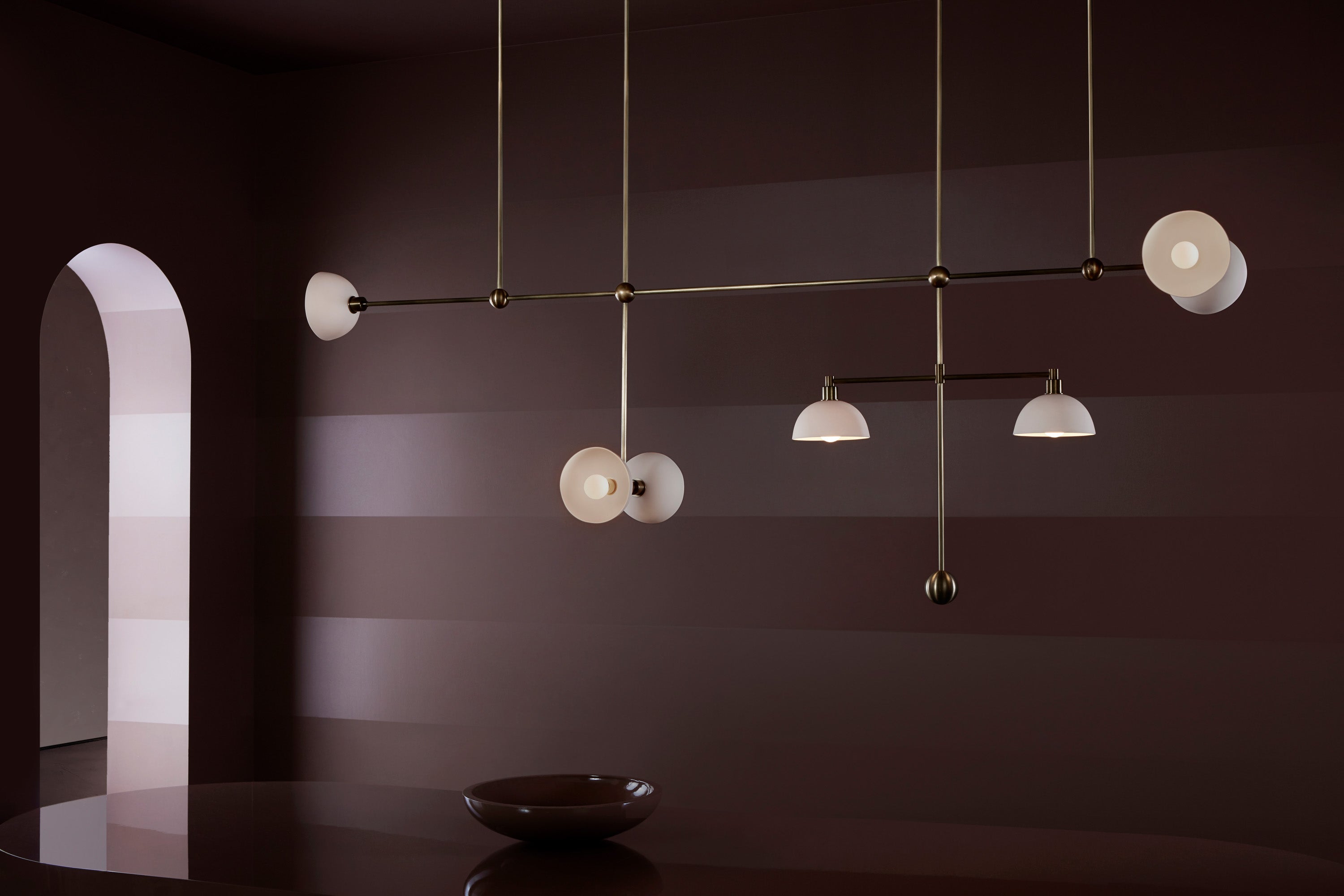 An illuminated TRAPEZE : 7 MOBILE ceiling pendant in Aged Brass with Porcelain bowls. 