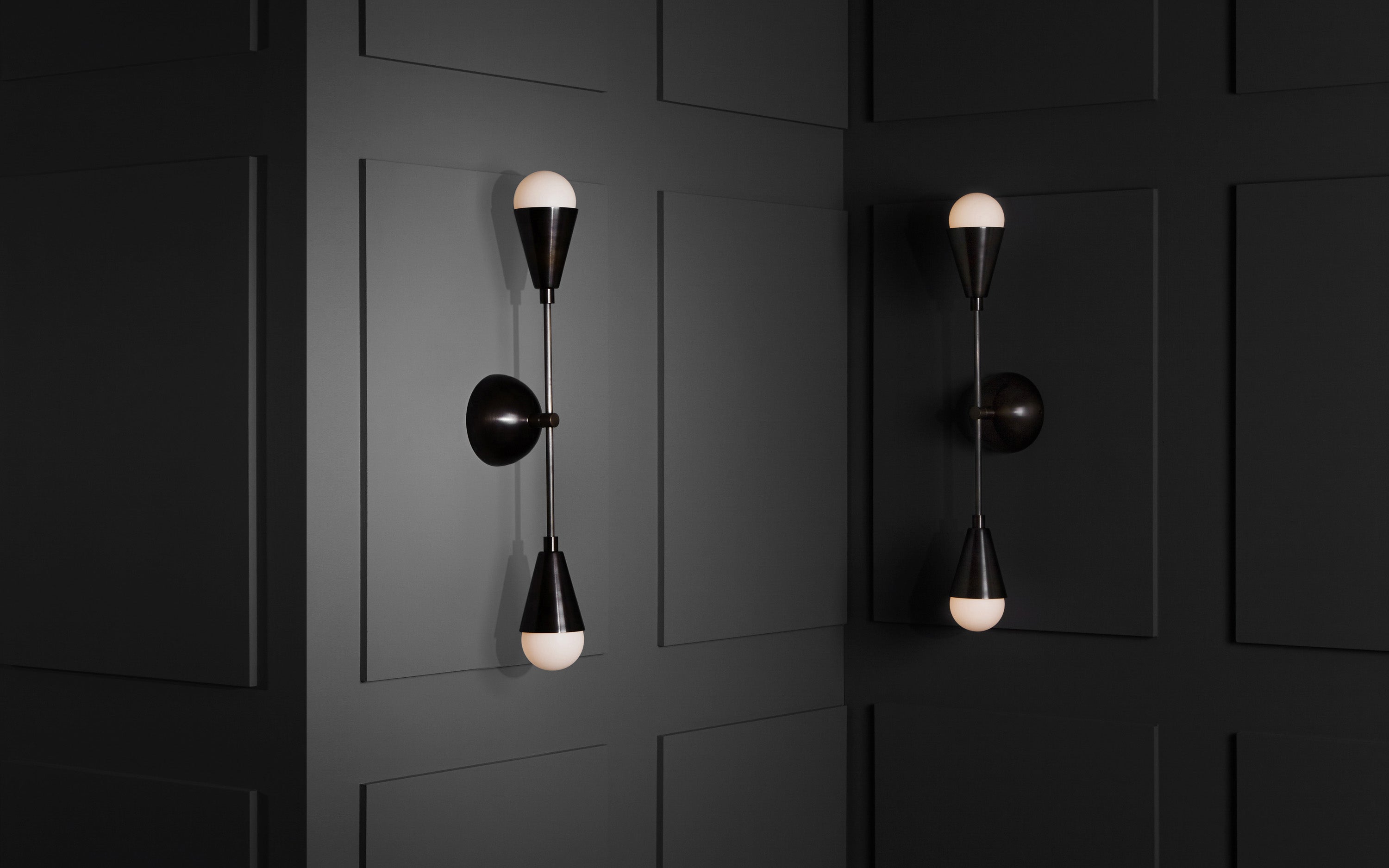 A pair of TRIAD : 2 sconces mounted vertically to a paneled wall. 