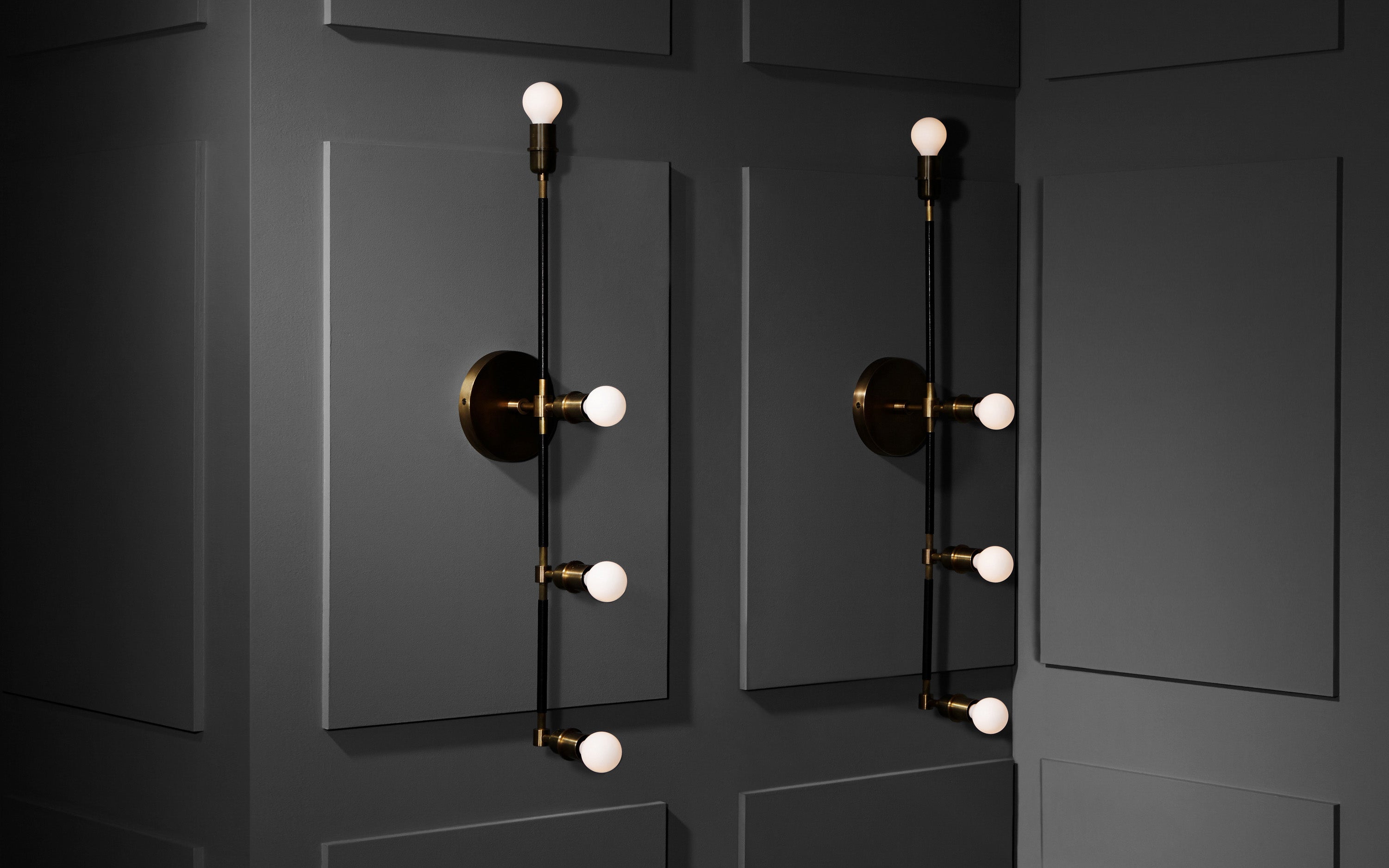 A pair of VANITY sconces in Aged Brass finish with Black Leather mounted to a white paneled wall.