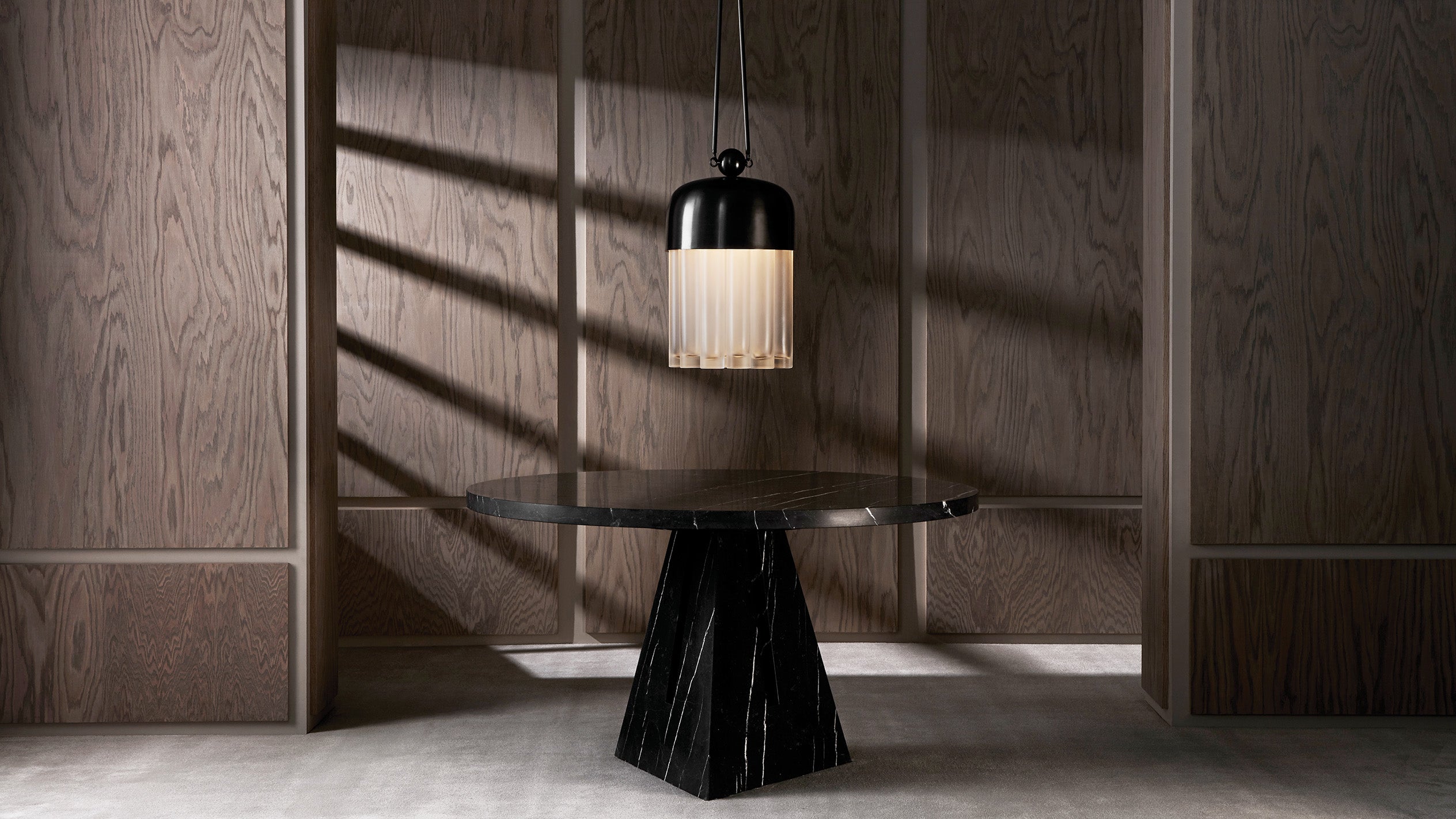An illuminated TASSEL : 19 ceiling pendant hanging above a circular PORTAL dining table.
