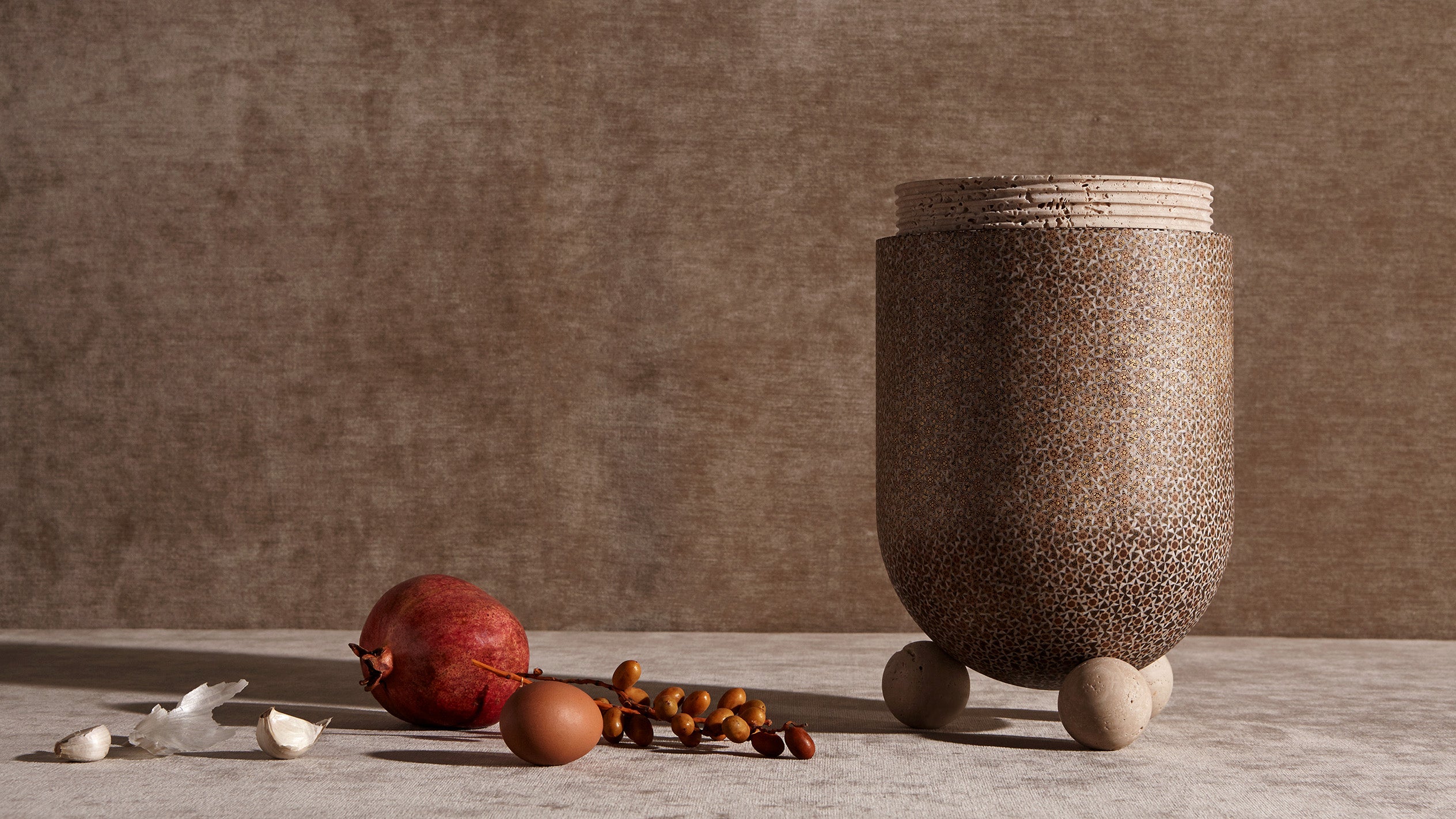 A decorative object sitting next to garlic cloves and an assortment of fruits.