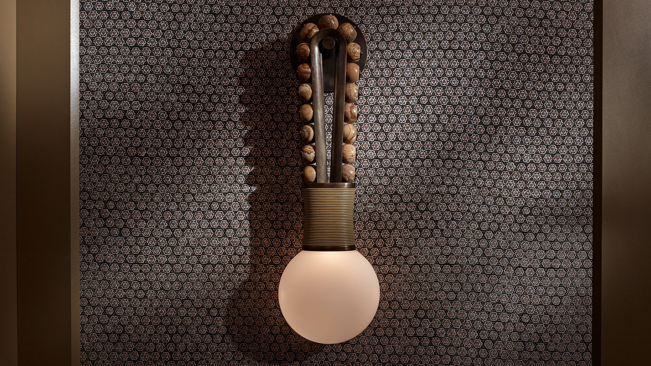 An illuminated TALISMAN : LOOP SCONCE mounted to a textured wall. 