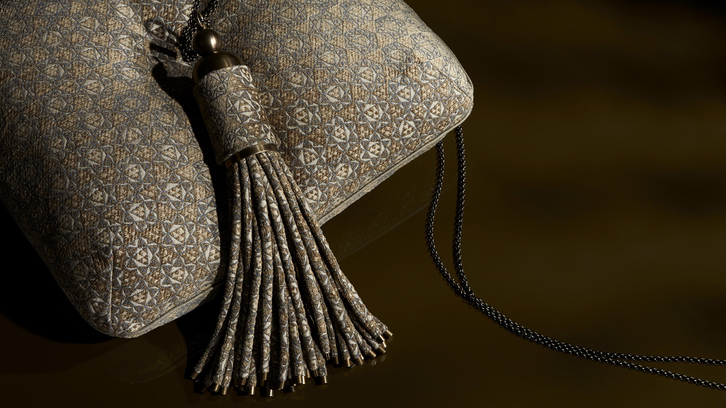 Close up of a tassel and cushion showing details of the patterned upholstery. 