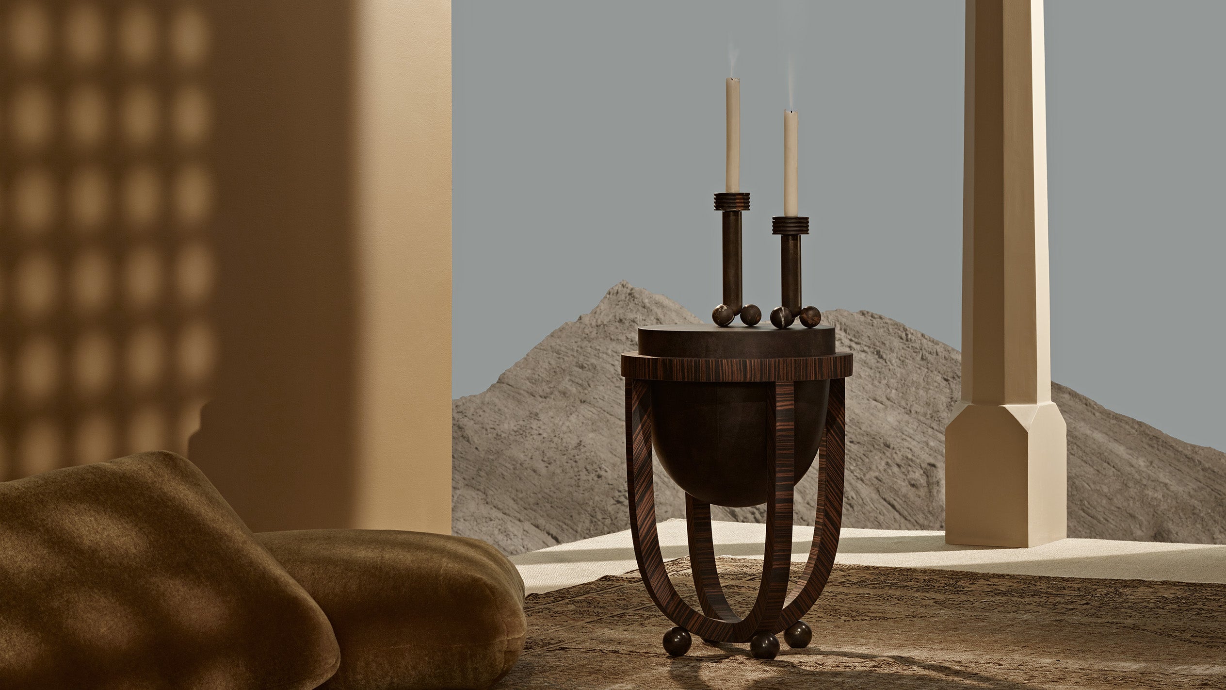 A pair of decorative candle stick holders on an end table with a desert scene in the background. 