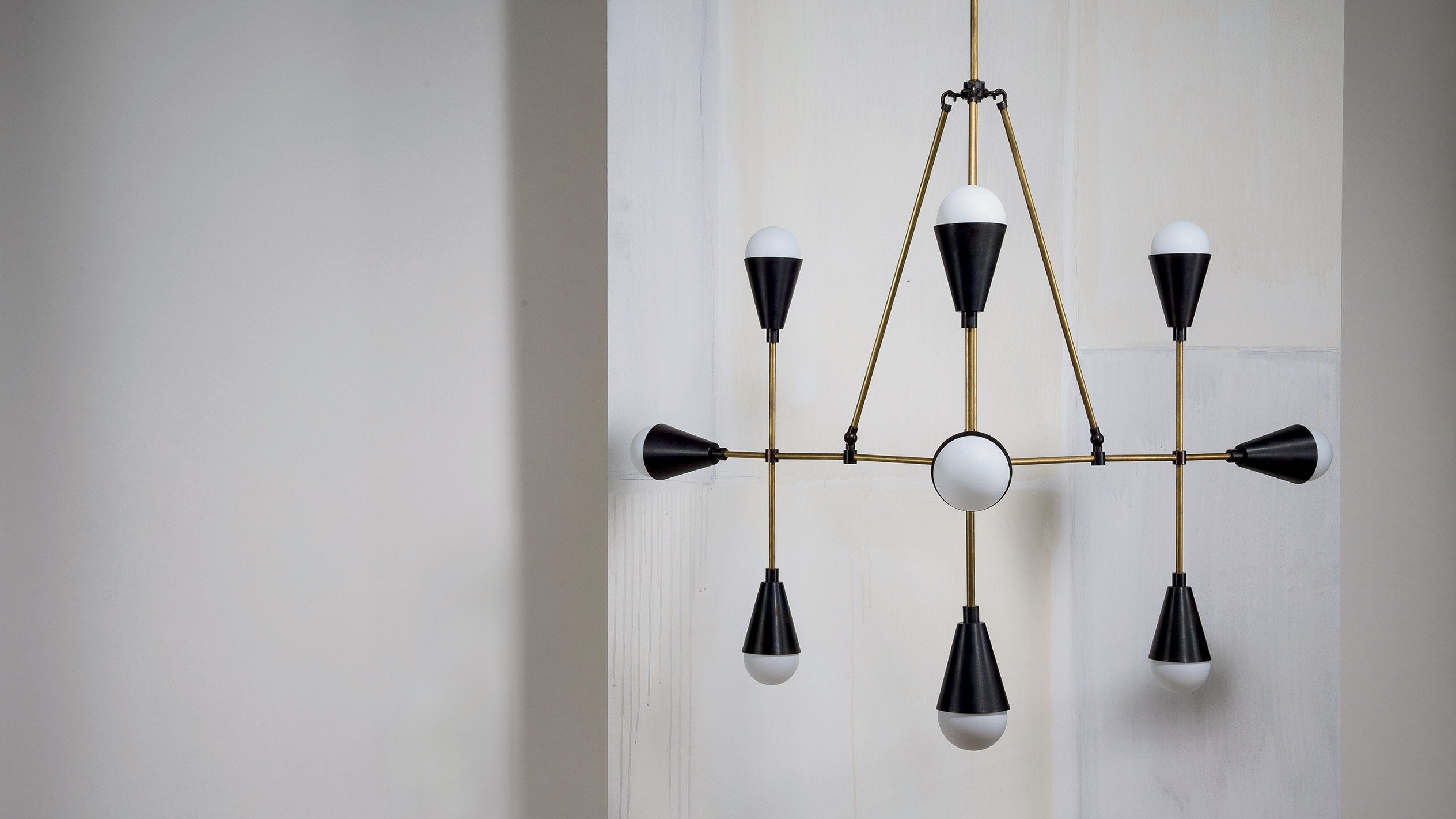 TRIAD : 9 ceiling pendant in Blackened Brass and Aged Brass, hanging against a white wall. 