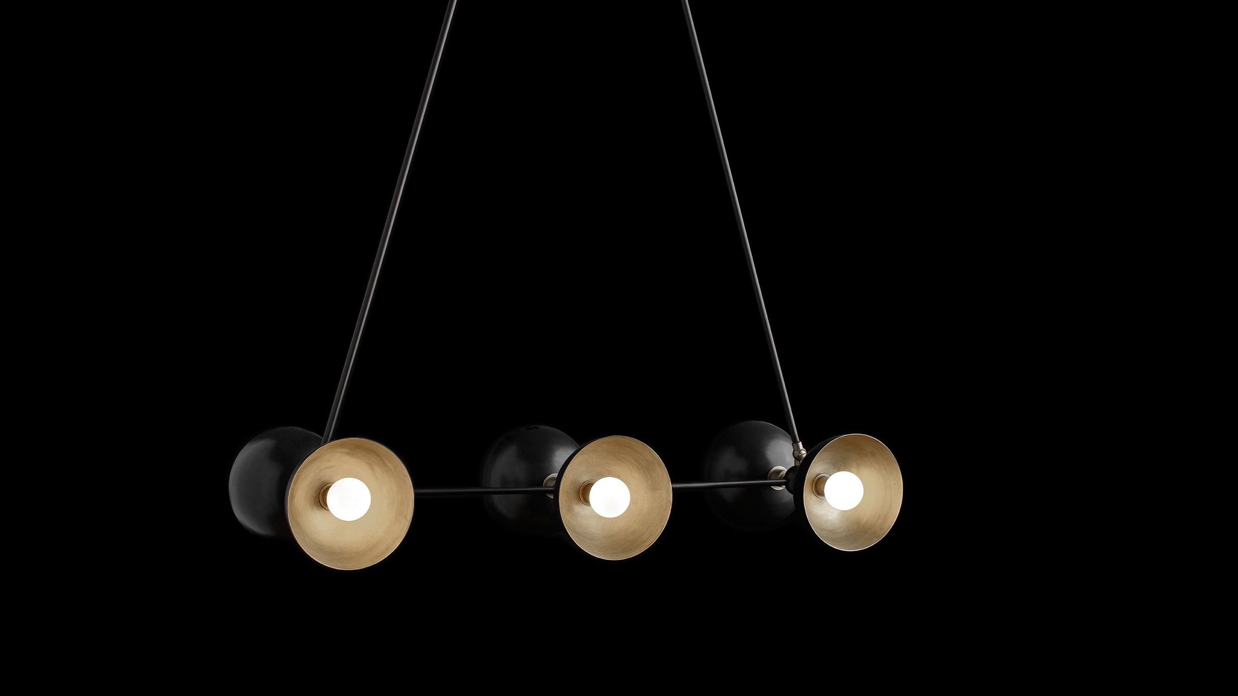 TRAPEZE : 6 ceiling pendant in Blackened Brass finish with Aged Brass bowls, hanging against a black background. 