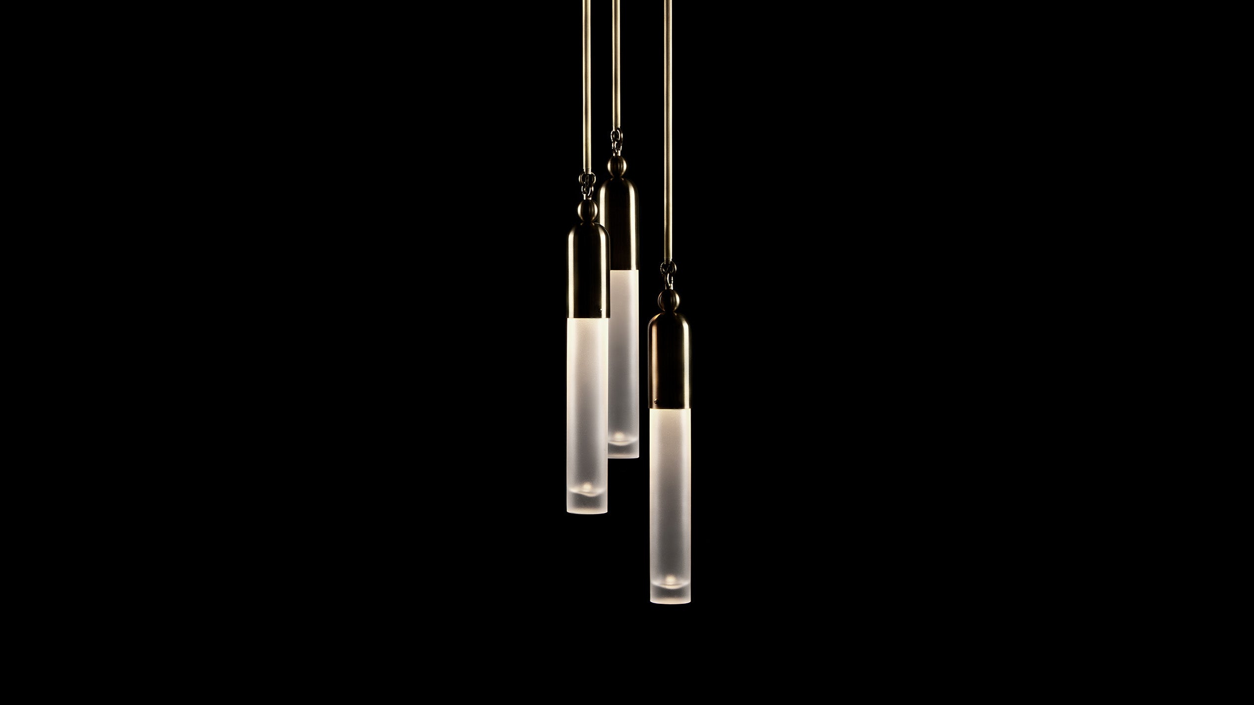 An installation comprising of three TASSEL : 1 pendants in Oil-Rubbed Bronze hanging at different heights, against a black background. 