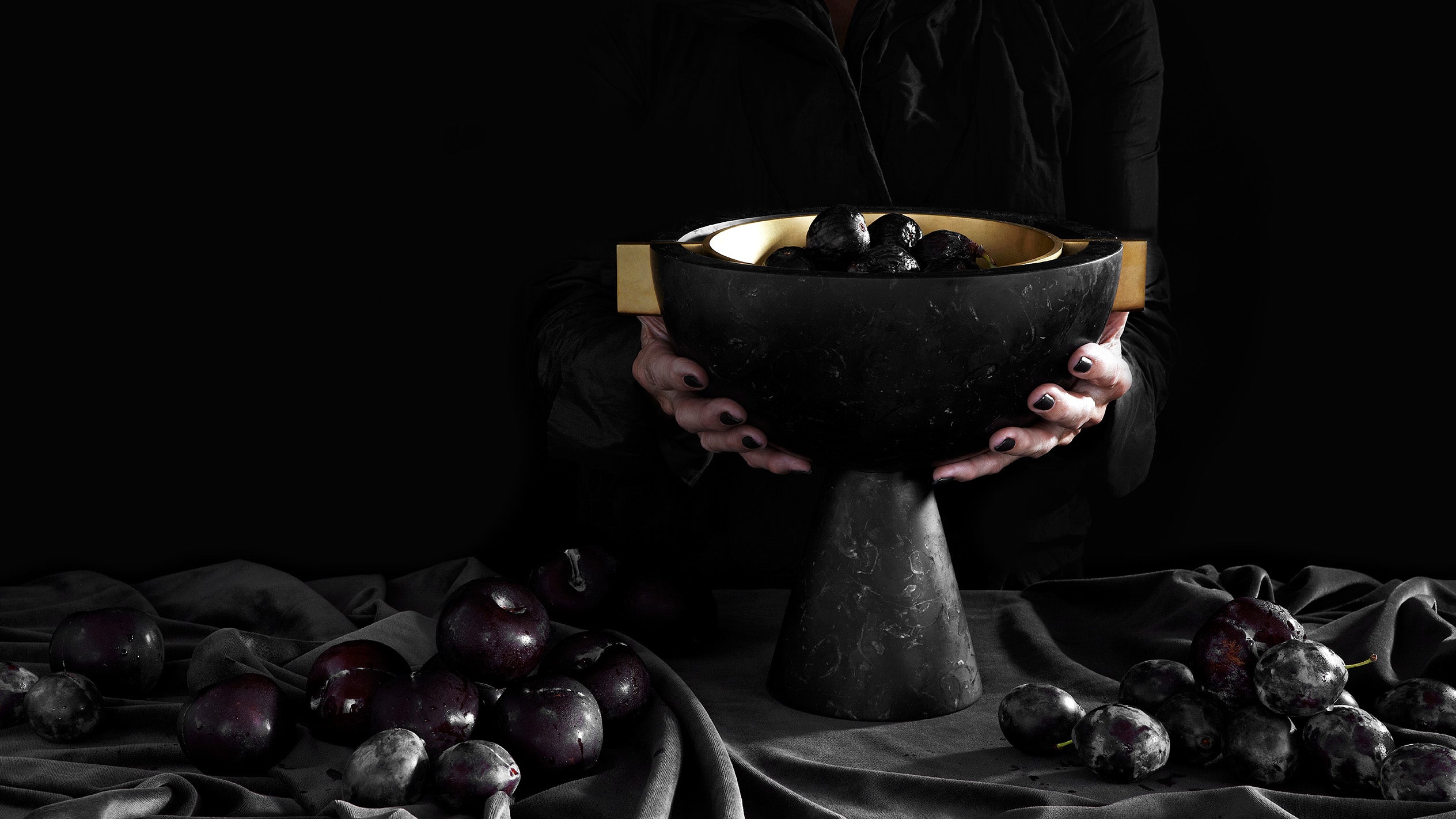 A pair of hands with black painted finger nails holding NEO VESSEL in Nero Kinitra Marble, a decorative object used for burning incense.