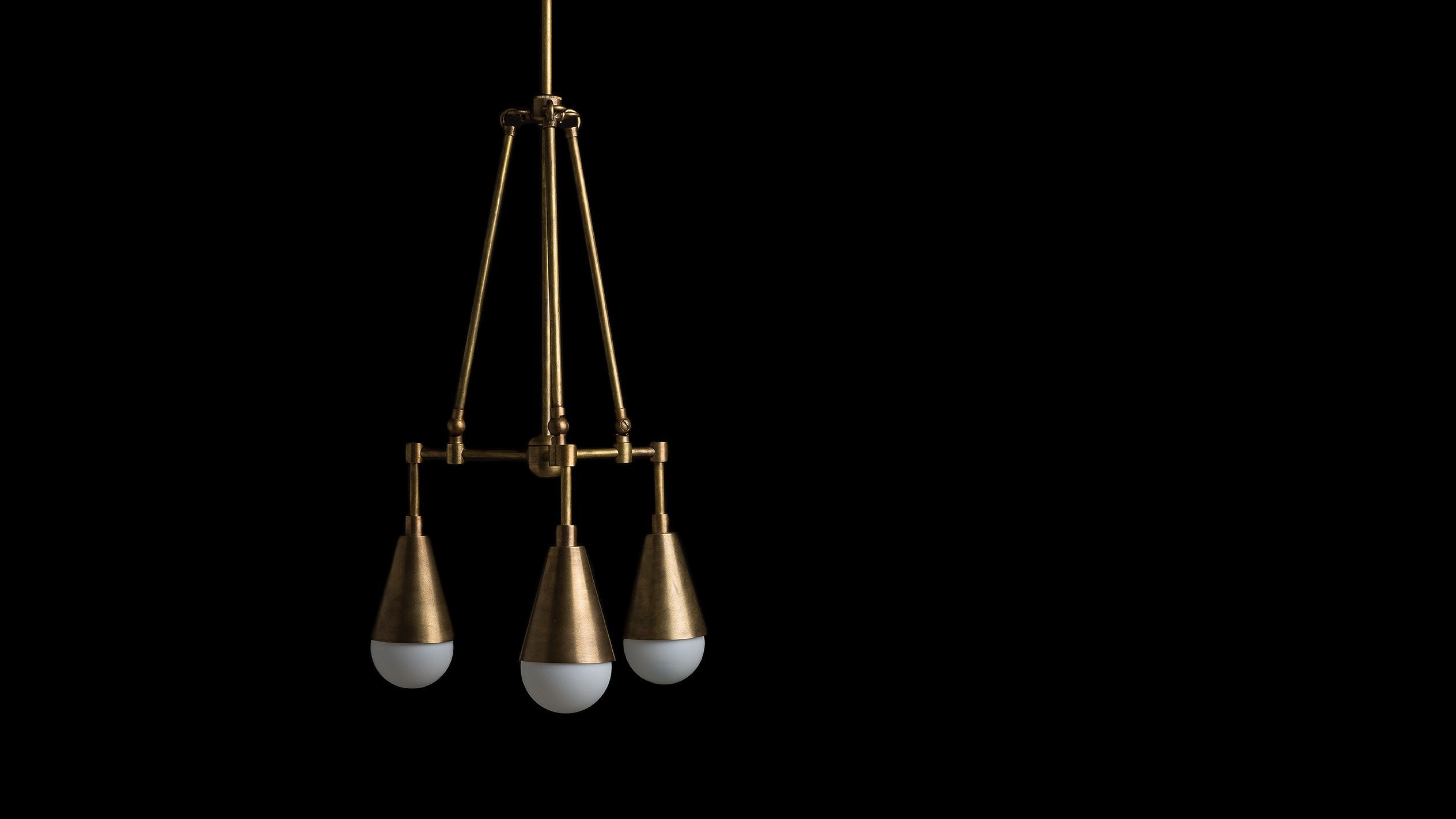 TRIAD : 3 ceiling pendant in Aged Brass finish, hanging against a black background. 