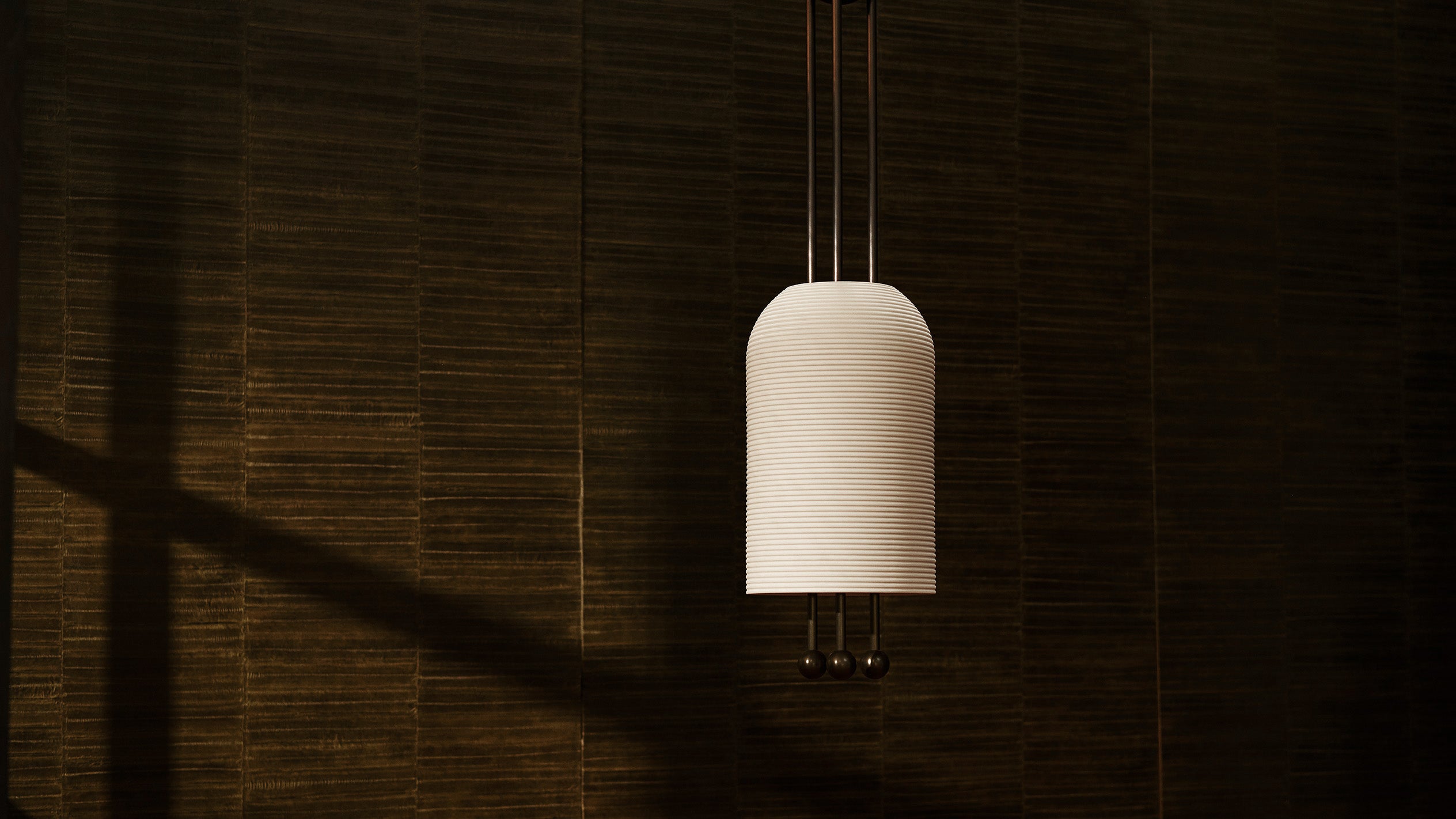 LANTERN ceiling pendant in Aged Brass and Blackened Brass finish hanging in front of a textured wall. 