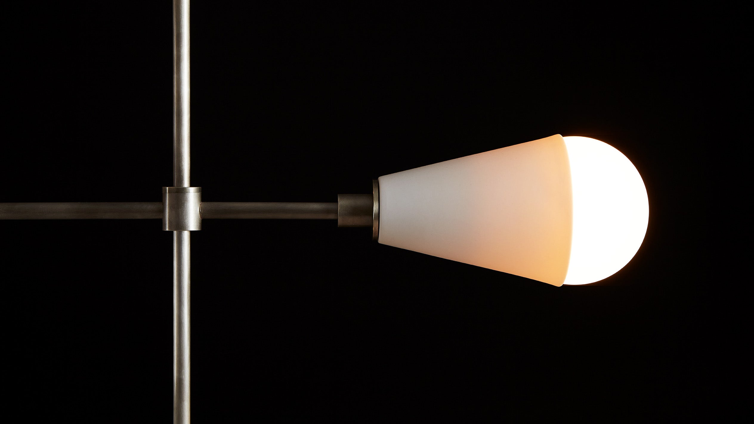 Close up of an illuminated TRIAD : 9 LINEAR ceiling pendant showing details of the Aged Brass finish, Tarnished Silver finish and Porcelain. 