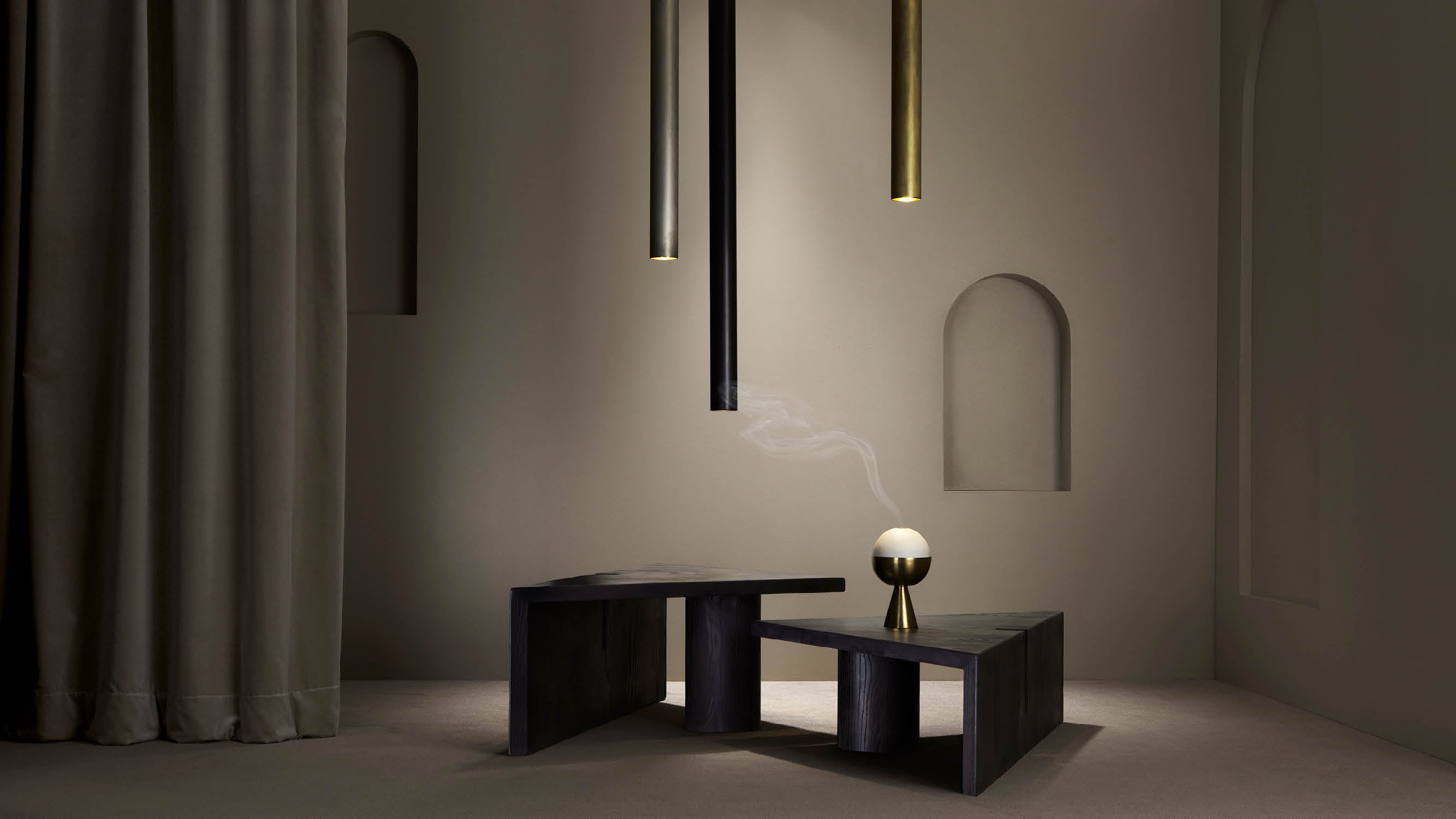 A decorative object used for burning incense sits on top of a modular PORTAL coffee table in Blackened Ash Wood, under a trio of CYLINDER ceiling pendants in an assortment of metal finishes. 