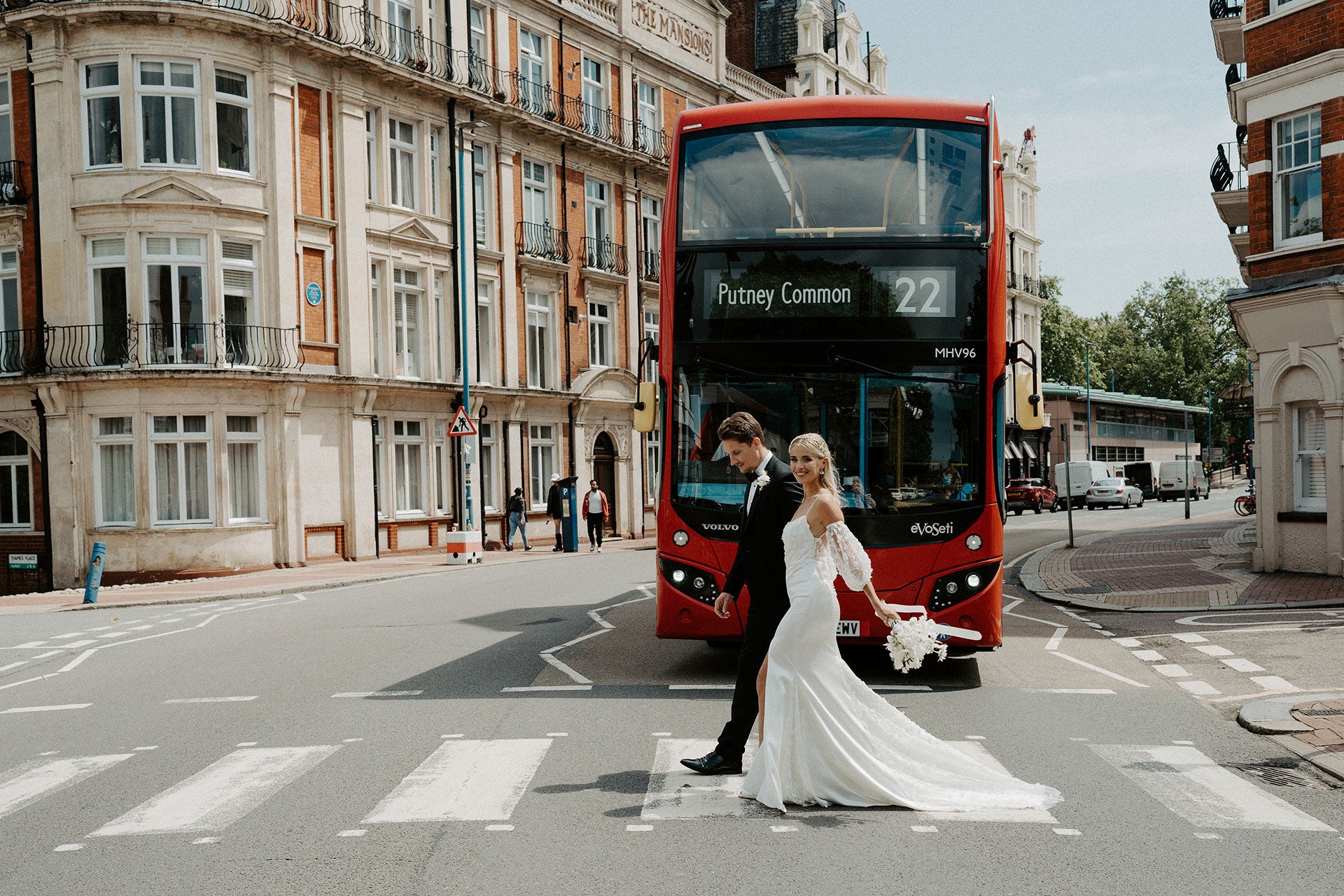 Newlyweds crossing a zebra-crossing in front of a red London bus