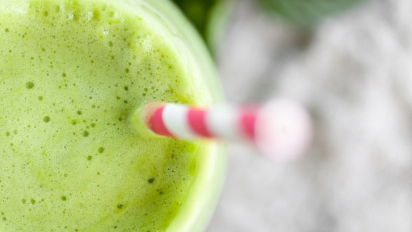 zoomed in shot of the top of a green smoothie with a red and white paper straw