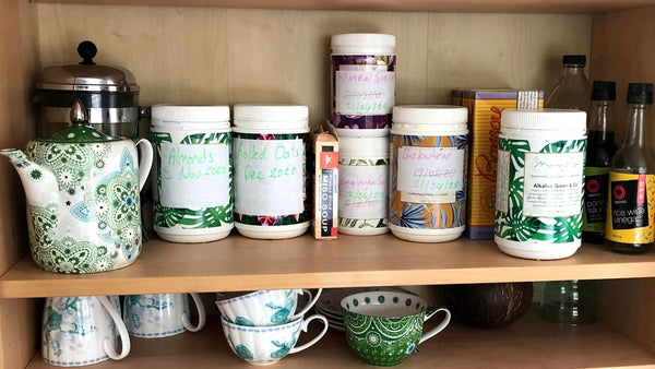 mayella containers in a pantry reused for pantry staples and relabelled by hand above a shelf of tea cups