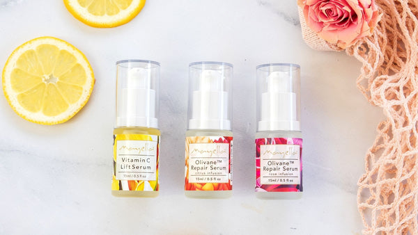 three Mayella serums in glass containers lying flat on a marble bench next to slices of lemon