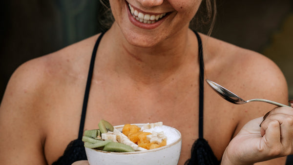 smiling woman eating a fruit and yogurt bowl