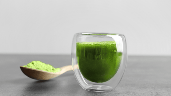 clear espresso glass filled with green liquid next to a spoon of greens powder