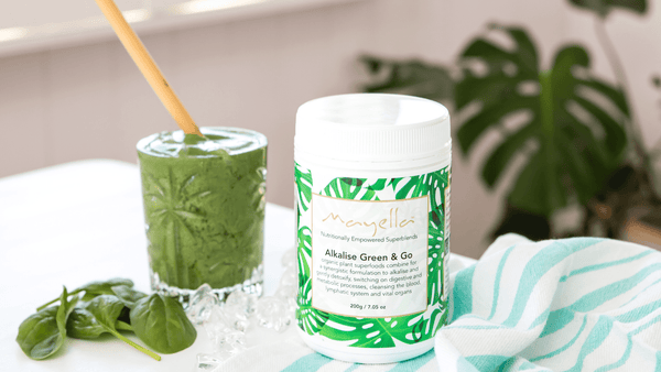 tub of alkalise green and go next to a green smoothie in a glass with a bamboo straw inside