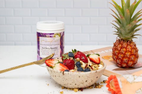 Mayella Acai Berry Beautiful container sitting on a bench next to a smoothie bowl made with Acai Berry Beautiful and topped with an abundance of fresh fruits