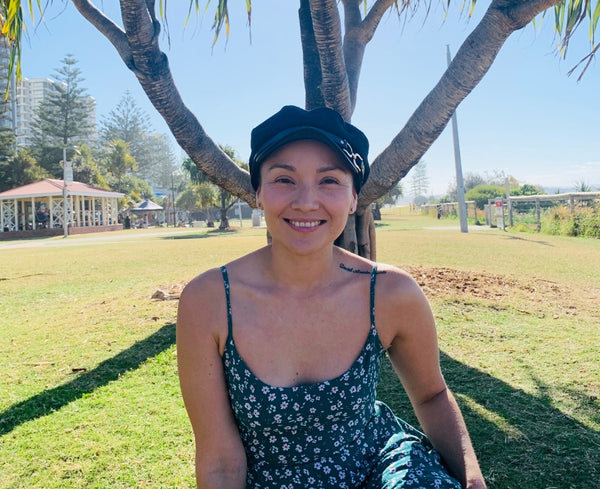 Lorena sitting outdoors in a park with a hat on an smiling