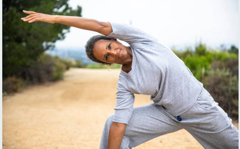 Mature woman in fitness clothing outside in nature stretching to her right side exercising