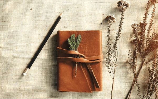 leather-covered journal on a hessian cloth next to wild flower foliage and a pencil