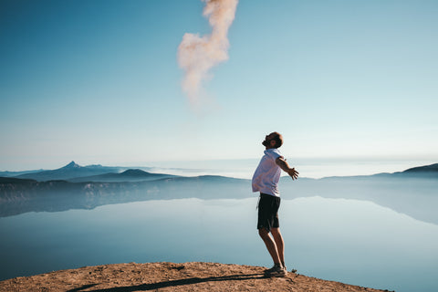 Person standing outdoors on hill overlooking water with arms outstretched breathing in deeply and surrounded by blue skies