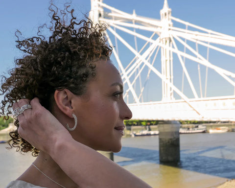 woman with curly hair standing in front of Thames river and a bridge