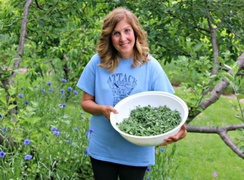 woman in blue shirt holding bowl of plants, standing in a garden