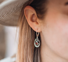 close up of swirly silver earring with pear shaped red garnet on woman's ear wearing a hat