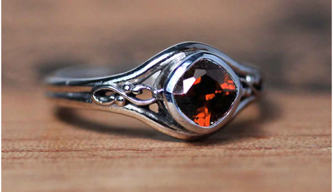 silver ring with square cushion cut red garnet set in a bezel with a sculptural infinity symbol on each side