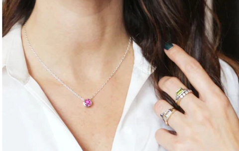 Picture of woman in white collared shirt, wearing a silver chain with a round pink bezel set gemstone