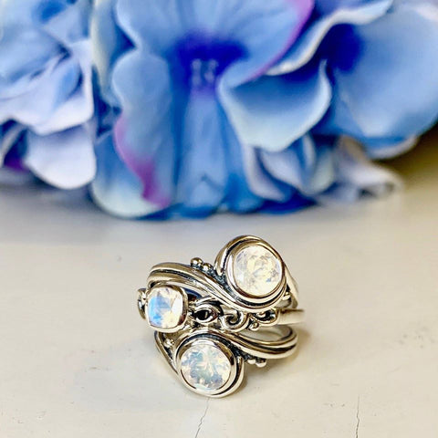 Three sterling silver and rainbow moonstone rings stacked up in front of blue flowers