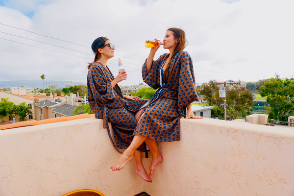 two women drinking a beer on a rooftop wearing robes as swim cover ups