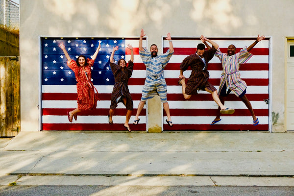 friends jumping in air in front of american flag wearing robes as a swim cover up