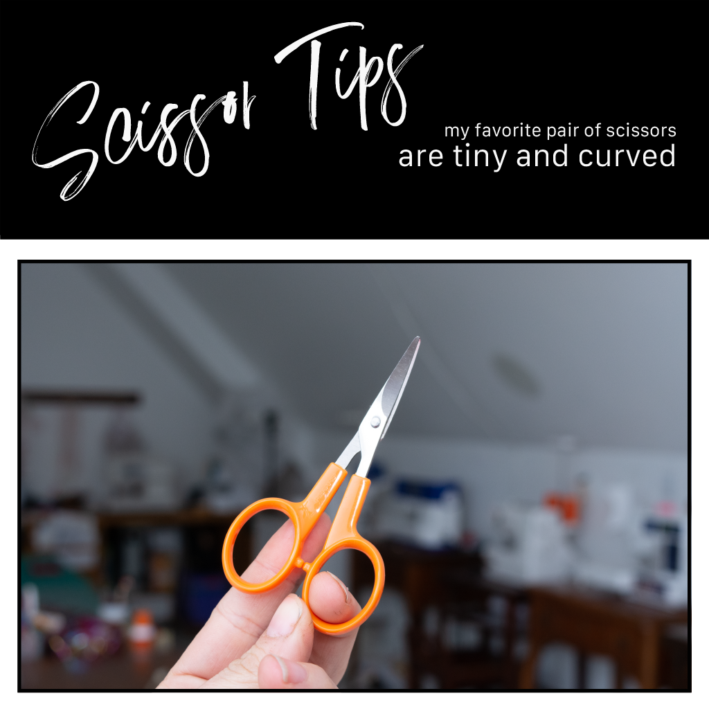 curved scissors held by a white hand with sewing machines in the background slightly out of focus