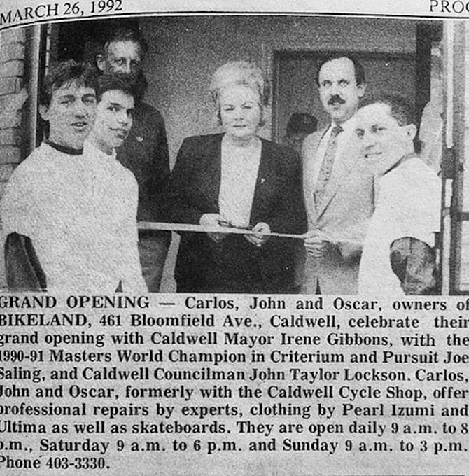 Picture of the Bikeland USA Grand Opening in 1992 with the owner and town officials in front of the bike shop cutting a ribbon to the entrance of the bike shop.