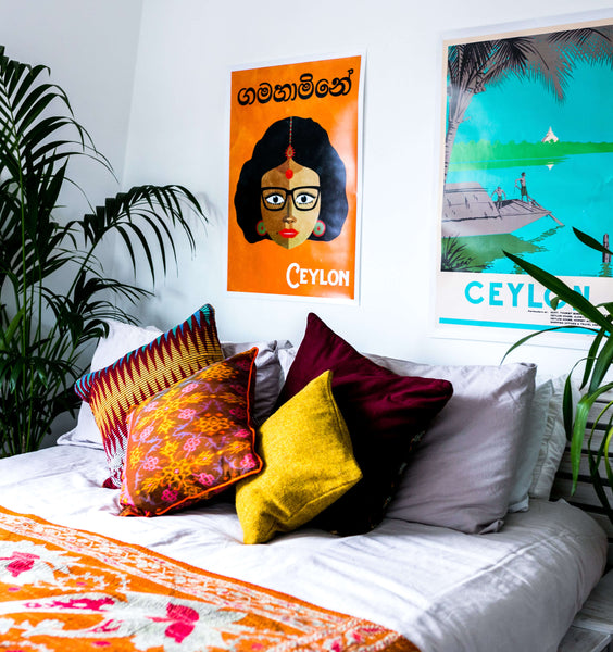 Handmade Ikat and Bhutanese cushions on a white bed with plants and posters in the background