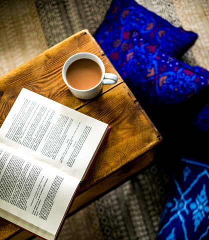 A table with an open book and a cup of coffee with blue cushions in the background