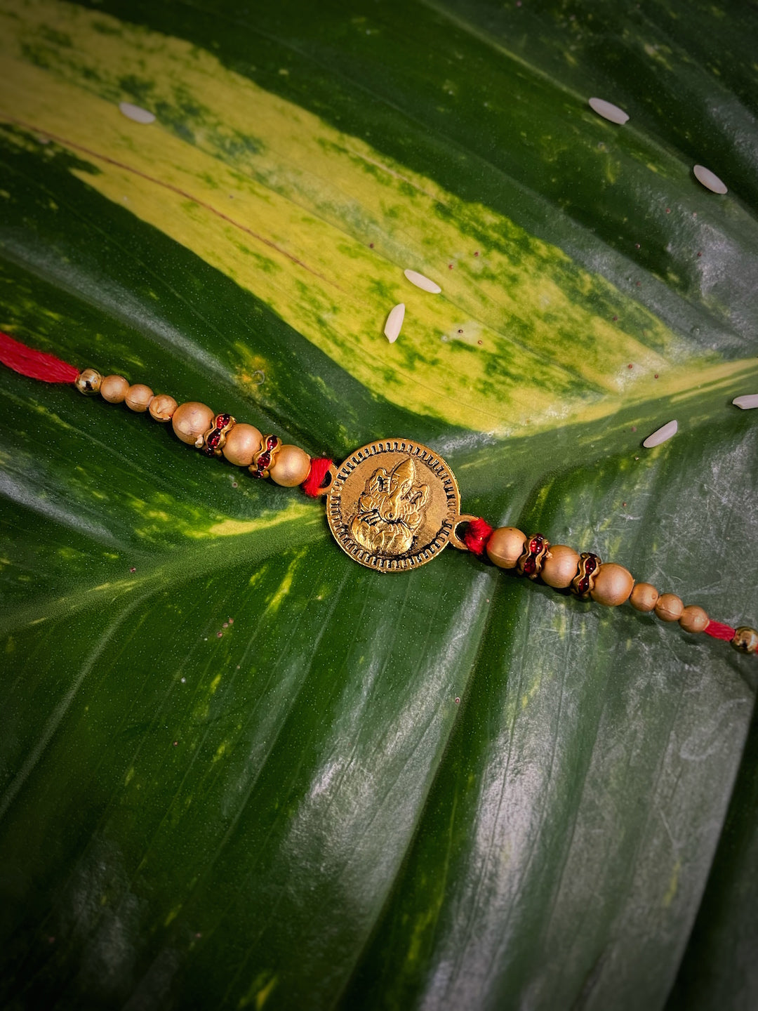 image for Beautiful Designer Ganesha Engraved On Coin With Gold Beads & Red Thread Rakhi For Raksha Bandhan