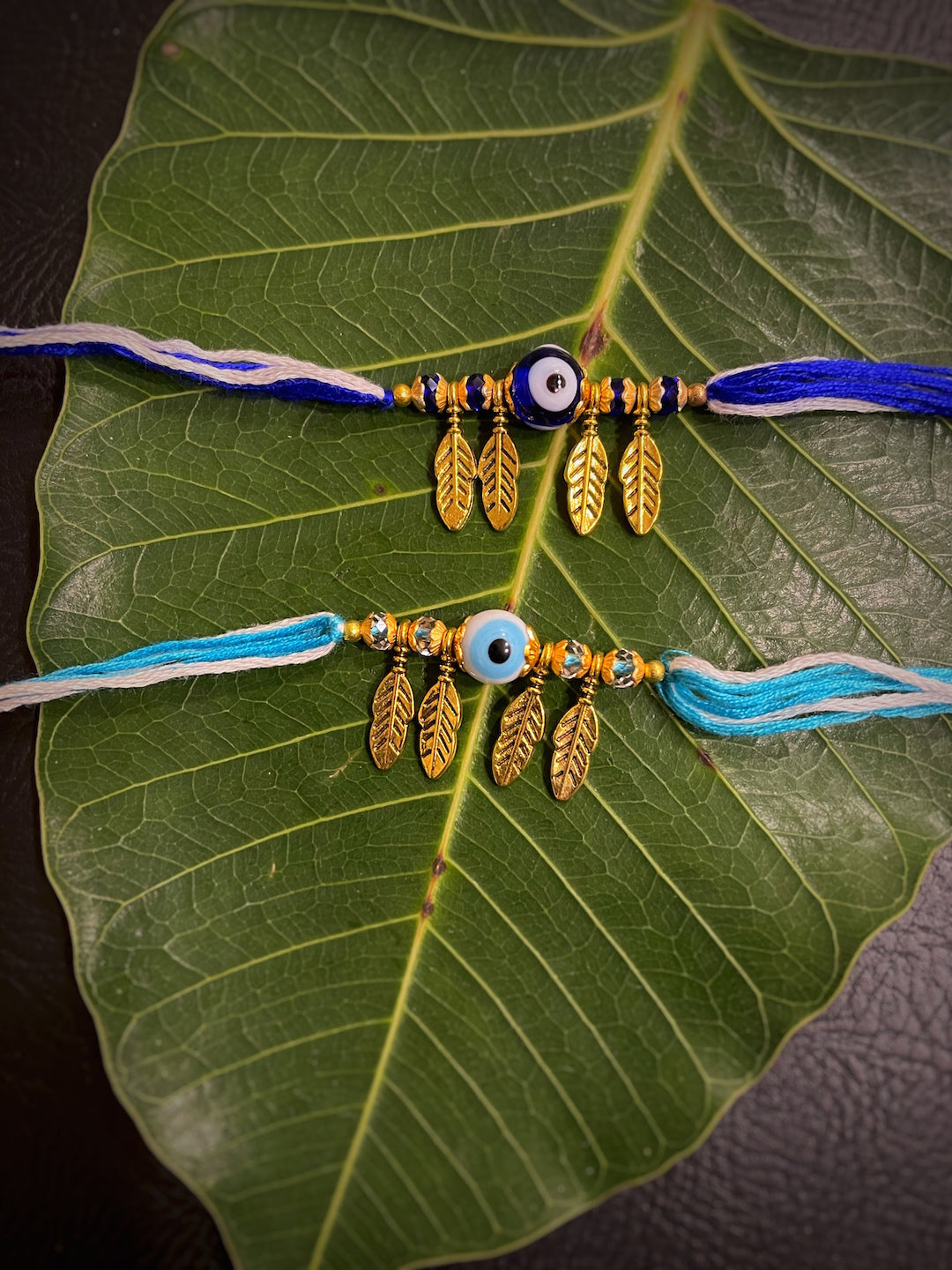 image for (Combo of 2) Fancy Round Evil Eye Rakhi Designs Leaf Pattern Pendant Blue/White Mauli Raksha Bandhan