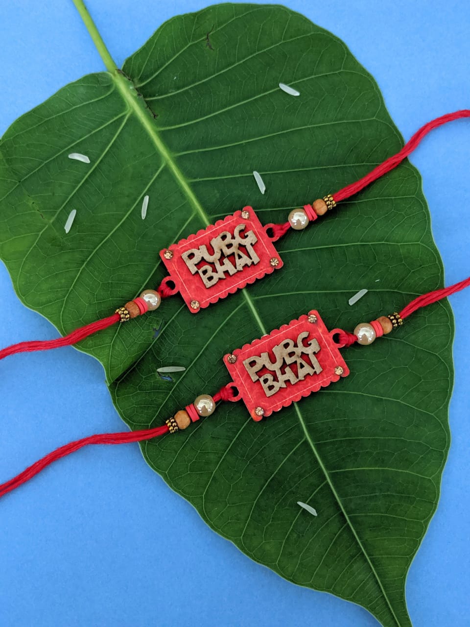 image for (Set of 2) Fancy PUBG Rakhi Set with Pubg Bhai Slogan White Pearls Tulsi Beads Red Thread Rakhi Combo