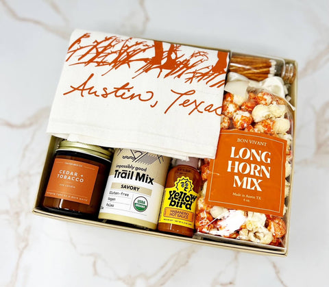 we love austin gift box with longhorn tea towel, longhorn mix popcorn, matches, yellowbird hot sauce, shar trail mix, and cedar + tobacco candle
